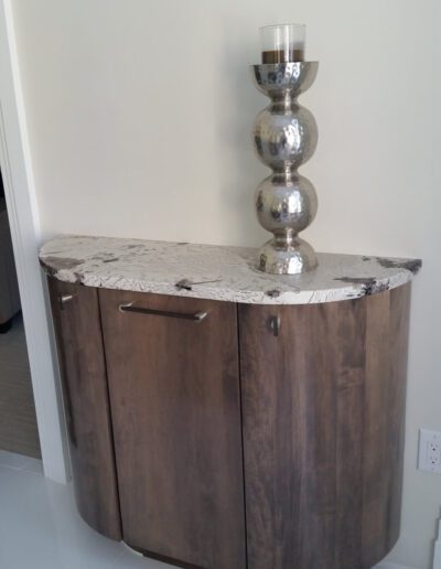 A half-round wooden cabinet with a patterned countertop and a decorative silver lamp placed on top.