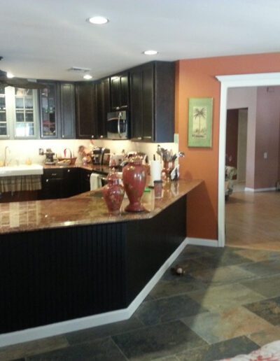 A spacious kitchen with dark cabinetry and a granite countertop island, featuring terracotta walls and tiled flooring.