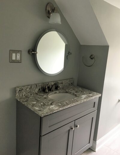 A modern bathroom vanity with a marble countertop and round mirror.