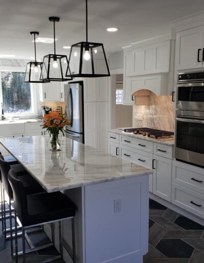 Modern kitchen interior with white cabinetry, stainless steel appliances, and a central island with bar stools under pendant lighting.