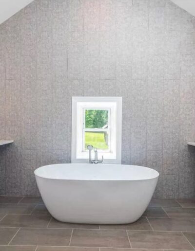 Modern bathroom with a freestanding tub, double vanity, and a view of greenery through the window.