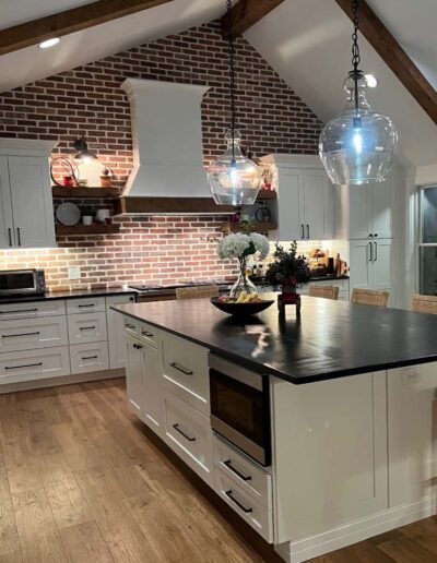 A modern kitchen with white cabinetry, a central island, exposed brick details, and pendant lighting.