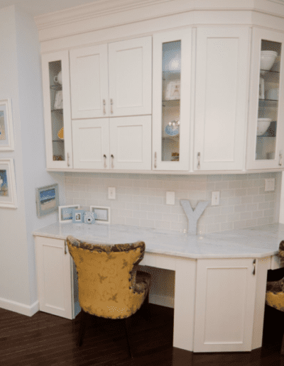 A cozy kitchen nook with white cabinetry, a small desk area, and two upholstered chairs.