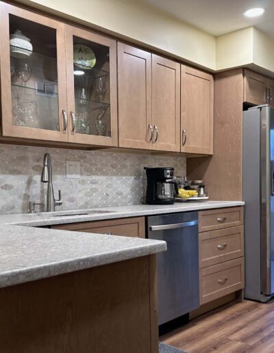 Modern kitchen interior with wooden cabinets, stainless steel refrigerator, and granite countertops.