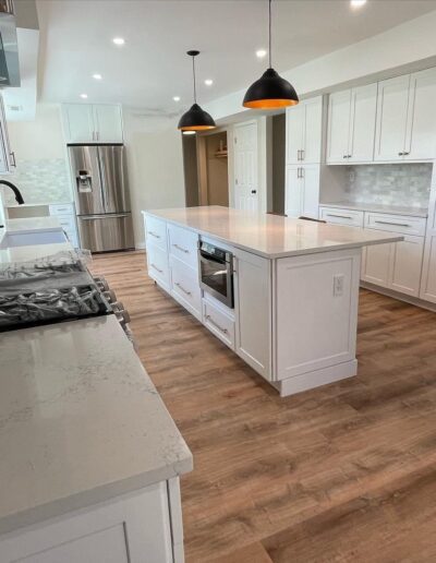 Modern kitchen with white cabinets, a large island, stainless steel appliances, wood flooring, and three black pendant lights hanging above the island.