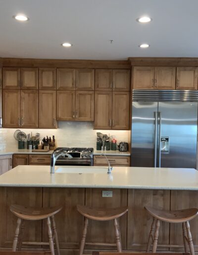 Modern kitchen with wooden cabinets, stainless steel appliances, and an island with four stools. A vase with red flowers is on the counter.
