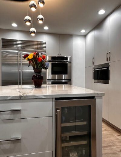 Modern kitchen with white cabinets, a marble island, stainless steel appliances, and overhead pendant lights. A vase with colorful flowers is placed on the island.