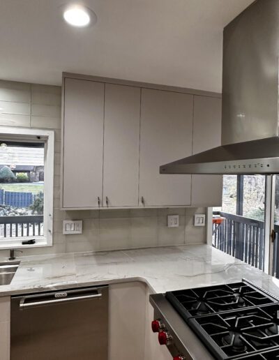 Modern kitchen with a gas stove, stainless steel range hood, and white cabinets. Rearranged with an adjacent sink and window showing an outdoor view.